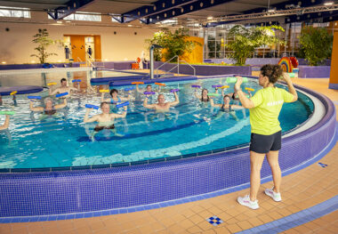 Gymnastiktrainerin am Beckenrand. Im Wasser trainieren Kursteilnehmer