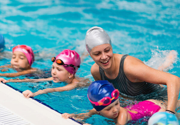 Schwimmtrainerin mit Schwimmschülern im Wasser am Beckenrand